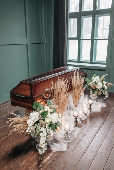 A floral arrangement featuring white roses, hydrangeas, and green foliage, complemented by tall, beige pampas grass, displayed in two matching bouquets arranged on either side of a vintage wooden cask
