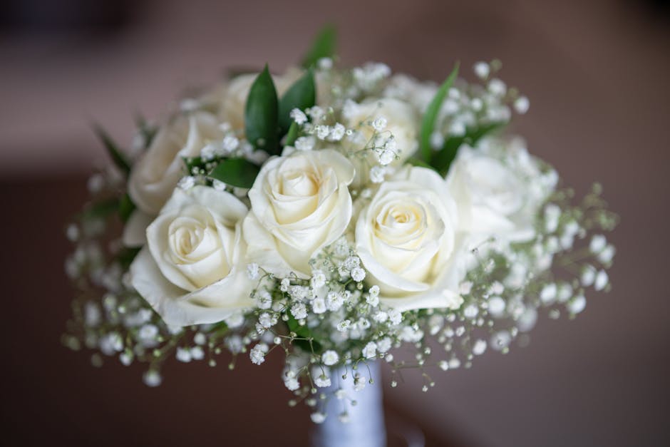 A close-up image of a floral bouquet from AddingtonFlowers.org.uk featuring creamy white roses arranged in a compact, rounded style. The bouquet includes delicate sprigs of baby's breath interspersed 