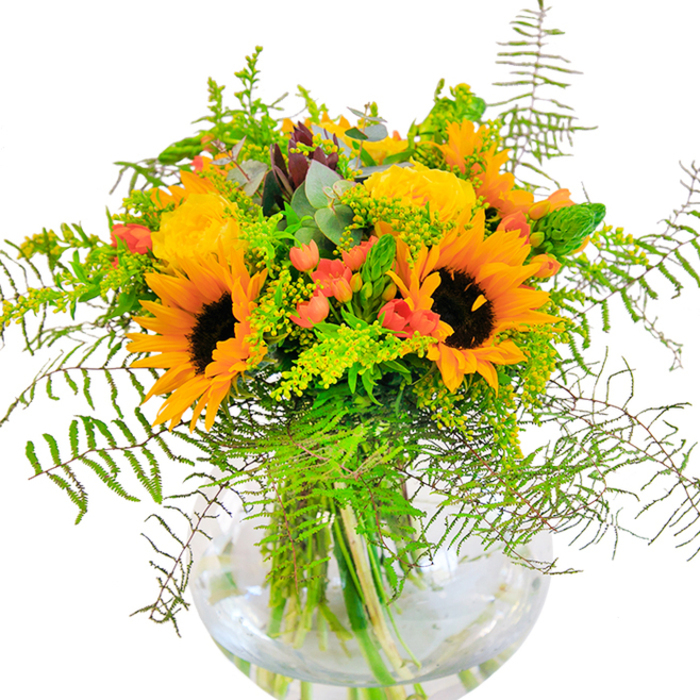 This exuberant bouquet radiates sunlight and celebration, its vibrant composition capturing the unmistakable essence of Addington in bloom. At its heart, resplendent sunflowers stretch arching petals of yellow and orange, their dark brown centers echoing the fertile soil of the local commons. Interlaced among them, plush yellow garden roses unfurl in opulent spirals, adding a touch of refined sophistication. Accenting the design, fresh scarlet Hypericum berries gleam amid sprays of lush greenery, their density and color reminiscent of ripening berries along Addington's hedgerows. The bouquet's verdant filler, feathery fern fronds, and airy goldenrod enhance the natural sense of movement, their lines sweeping and playful, as if swaying in the gentle breeze by Addington Palace grounds. Touches of bluish-green eucalyptus introduce subtle nuance, their oval leaves peeking through with understated beauty. All stems are artfully gathered into a broad, round glass vase-a vessel both modern and classic, where water magnifies the clustered greens and anchors the composition. Up close, every petal and leaf sings with delicate contrast and textural interplay, whispering of open gardens and longer days. The bouquet's scent is softly floral with undertones of fresh greenery, evoking the first breath after rain or a morning stroll through local parks. A gift like this, available for same-day delivery by Addington Flowers, is perfect for milestones or everyday joys, enriching local homes with radiant color and a sense of communal happiness.